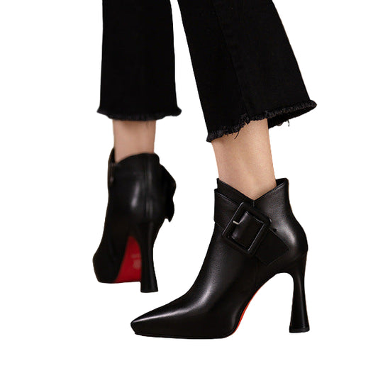 Black high-heeled boots with a red sole on a wooden floor.