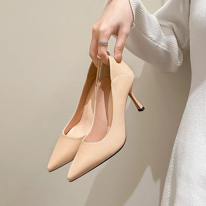 Beige high-heeled shoes held by a hand against a neutral background
