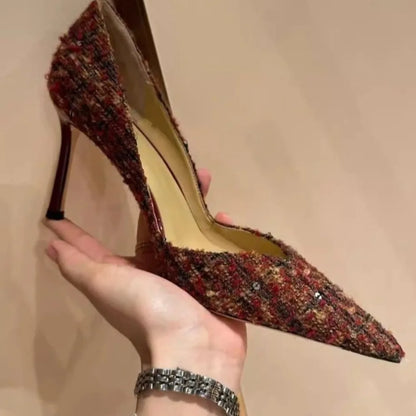 High-heeled shoe with a textured design held by a hand against a neutral background